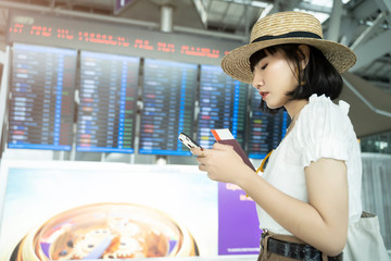 Young asian woman using mobile in airport for checking her flight boarding.