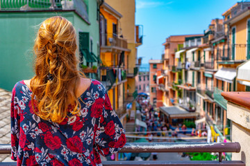 Young woman with red hair watching the amazing view of Manarola village in Cinque Terre, Italy. Sunny day and blue sky of an afternoon in the European summer. Unesco World Heritage Site
