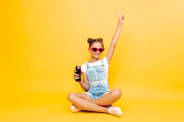 Portrait of a happy teenage girl resting on a yellow background with a refreshing drink in her hand