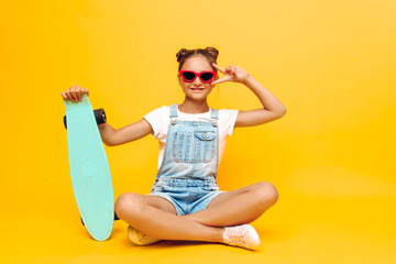 teenager sitting with skateboard, stylish girl posing in sunglasses on yellow background