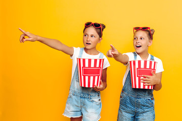 Two teenage girls, stylish girlfriends with popcorn in their hands, watching a horror movie on a yellow background