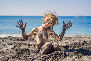 Black Friday concept. Smiling boy with dirty Black face sitting and playing on black sand sea beach...