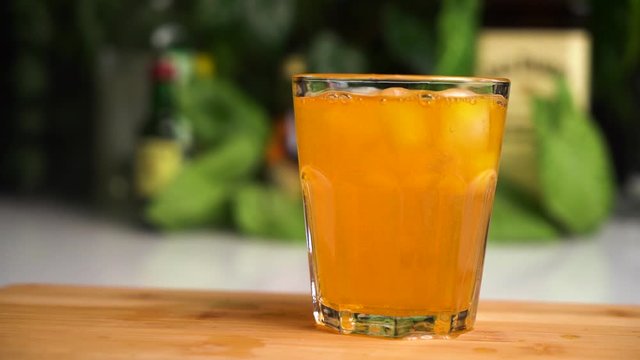 Ice cubes fall in glass of fanta or soda in slow motion with food background.