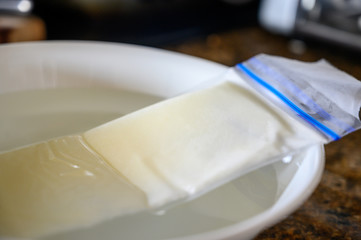 thawing frozen breast milk in bowl of warm water