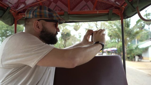 Happy man taking photo, recording video during tuktuk ride