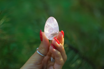 Female hand with red manicure holding transparent violet amethyst yoni egg for vumfit, imbuilding...