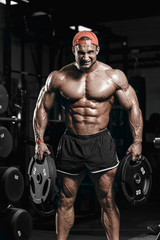 Fototapeta na wymiar Muscular athletic bodybuilder man hard training in gym over dark background with dramatic light with weights in strong pumped hands