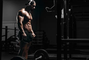 Foto op Plexiglas Muscular athletic bodybuilder man hard workout  in gym over dark background with dramatic light with barbell © Fotokvadrat