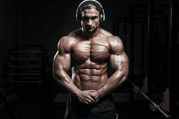 Muscular athletic bodybuilder man hard training in gym over dark background with dramatic light...