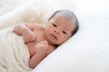 Medium shot 0-1 months beautiful cute asian newborn baby girl infant with black eyes and fragile skin lying down on the soft white baby sleeper blanket