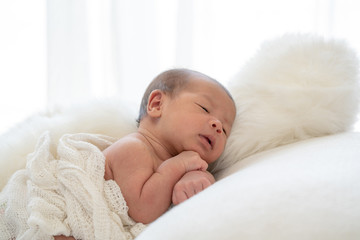 Medium shot 0-1 months beautiful cute asian newborn baby girl infant with black eyes and fragile skin lying down on the soft white baby sleeper blanket