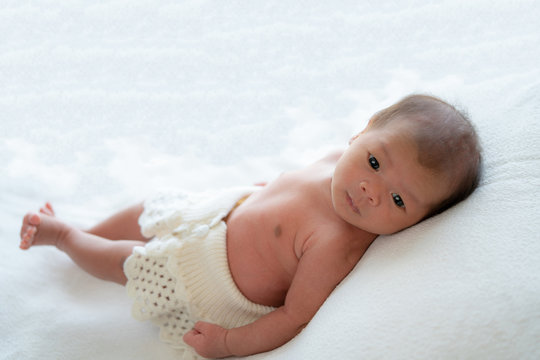 Medium shot 0-1 months beautiful cute asian newborn baby girl infant with black eyes and fragile skin lying down on the soft white baby sleeper blanket