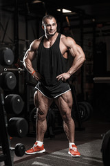 Naklejka na ściany i meble Muscular athletic bodybuilder man in gym over dark background with dramatic light posing and resting after hard training work out