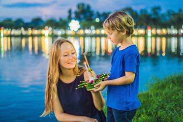 Mom and son tourists holds the Loy Krathong in her hands and is about to launch it into the water....