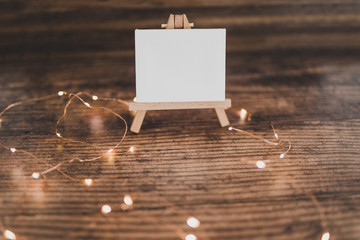 black canvas miniature surrounded by fairy lights on wooden desk with copyspace