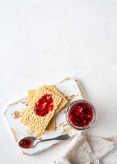 Toast crispbreads with raspberry jam served on wooden rustic board. Raspberry jam in a glass jar.