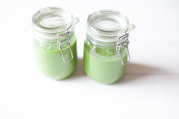 Healthy green smoothie in a glass jar on a white wooden background