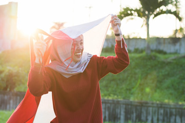 portrait of young asian muslim woman with scarf lift the red and white flag into the air