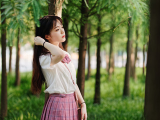 Portrait of beautiful Chinese girl in white shirt and pink skirt looking away with hand on hair in...