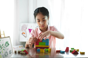 Little cute girl enjoy while playing wooden blocks toys on table at home