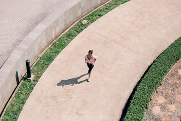 From above Asian female in sportswear running along concrete path in park during outdoor workout on...