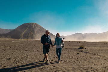 Fototapeta premium Happy couple travelers standing in a volcanic dusty desert near beautiful Mount Bromo in East Java, Indonesia