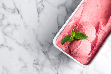 Container with delicious pink ice cream on marble table, top view. Space for text