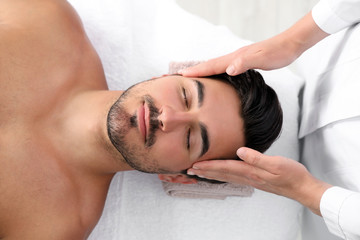 Fototapeta na wymiar Handsome young man receiving face massage on spa table, top view
