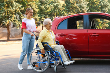 Senior woman in wheelchair with granddaughter near car outdoors