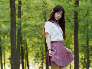 Portrait of beautiful Chinese girl in white shirt and pink skirt looking at camera with hands...