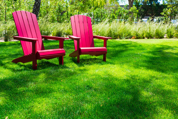 Traditional curveback sunset red plastic outdoor patio adirondack chairs with contoured backs and seats on green grass of outdoor lawn. Design, concept, idea