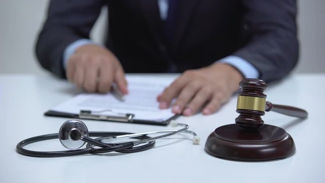 Judge signing arrest warrant for medical error, banging gavel near stethoscope