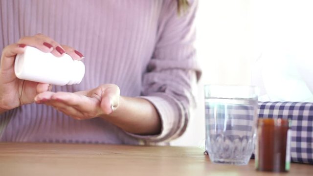 close up sick woman hand preparing to take medicine with glass of water and bottle of pill on desk 