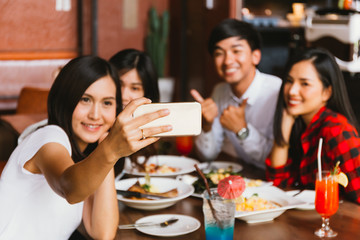 Group of Happy Asian male and female friends taking a selfie photo and having a social toast together in restaurant