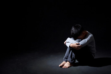 Asian Boy Sitting on Floor and Face Down on knee  ISOLATED on Black Background. Concept : Depressed. Disappointed. Emotion.