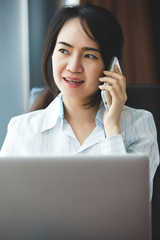 Happy asian business woman talking the phone at the working place.