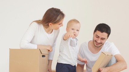 Family with a little boy unpacks cardboard boxes with Christmas decorations.