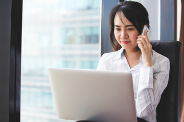 Asian business woman in smile face are using mobile phones and laptops in the office.