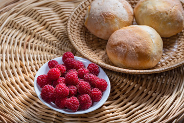 fresh red raspberries on a white saucer and tasty homemade buns on a wooden background