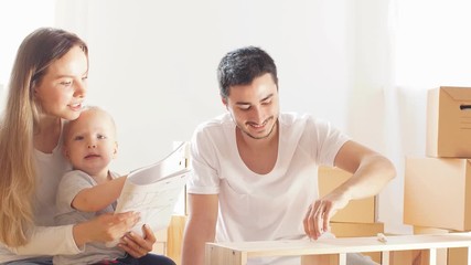 Happy young family with little boy reading instruction and assemble furniture together at living room of new apartment