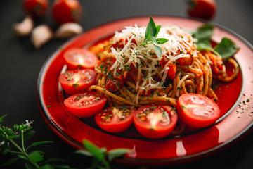 Spaghetti with cherry tomatoes, cheese and basil on dark table, close up 