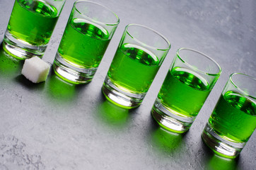 Absinthe green liquor in glasses. Alcoholic hallucinogenic beverage. Dark background. Pieces of...