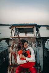A young woman sits with guitar on old abandoned ship.