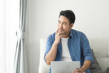 Fototapeta premium Stressed Asian man using laptop at home, lifestyle concept with copy space.
