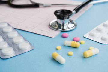 Pills, medical stethoscope, cardiogram on a light blue background. Cardiology concept. 