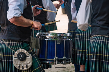 Closeup of the traditional Scottish drum and the hands of a drummer wearing kilt in Scottish band playing outdoors