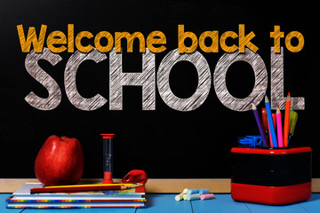 Text welcome back to school on black chalkboard with school accessories