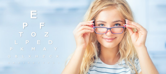 Portrait of young woman holding glasses and looking at camera. Ophthalmological concept with eye test chart