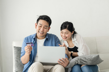 Fototapeta premium Happy Asian couple shopping online with holding credit card and laptop and sitting at home together, lifestyle