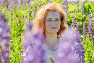Chubby middle-aged woman pensioner in a green field with flowers on a Sunny summer day